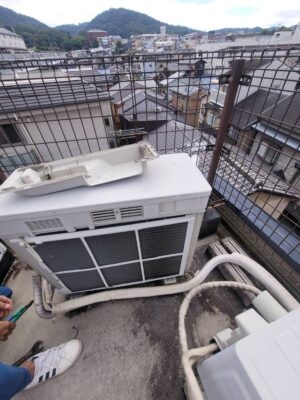 屋外に設置されたエアコン室外機と配管まわりで作業する職人